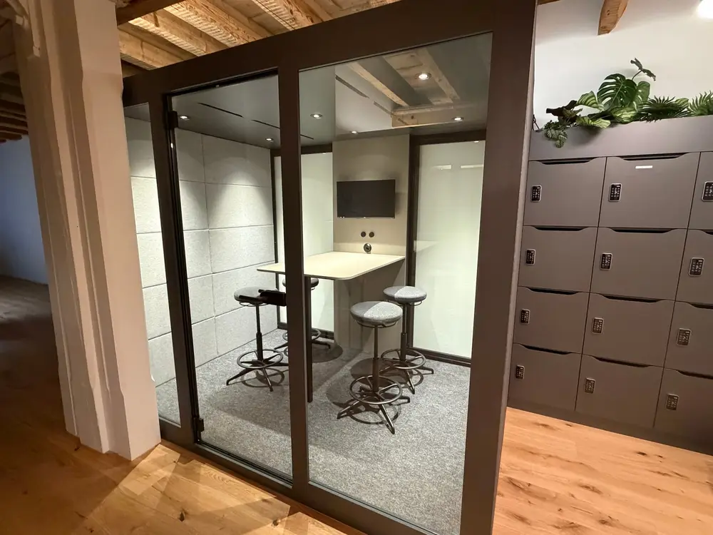 Verglaster Silent Room im G3ckarium mit Barhockern, daneben die Locker-Wand mit Pflanze